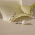 The Diamond Pearl Droplet Earrings in Sterling Silver are displayed beside a white calla lily on a beige surface.