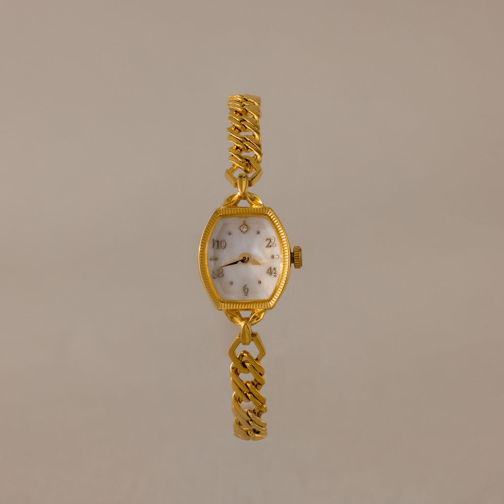 The Heirloom Chain Link Timepiece features a gold band and white oval mother of pearl dial, elegantly showcased on a neutral background.
