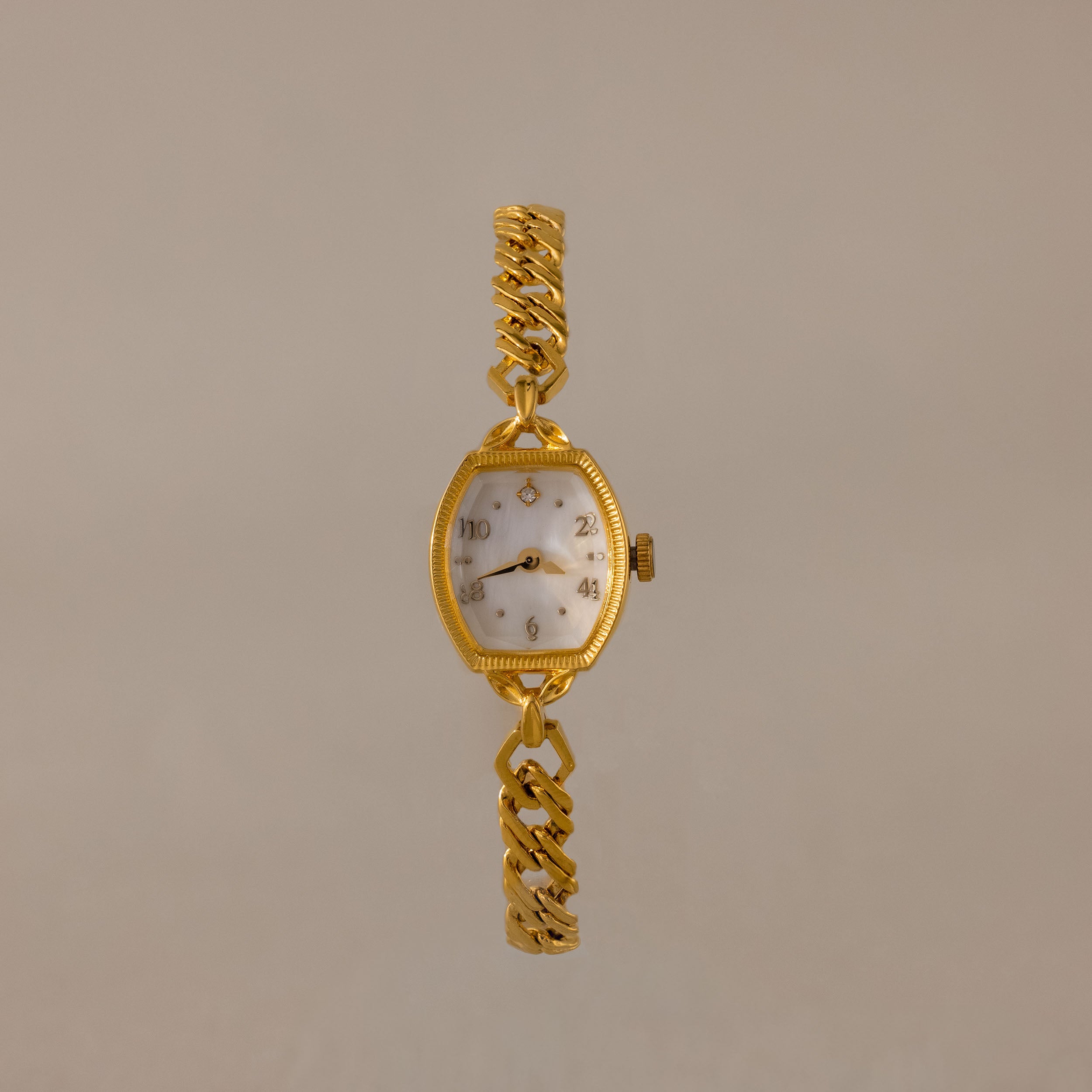 The Heirloom Chain Link Timepiece features a gold band and white oval mother of pearl dial, elegantly showcased on a neutral background.