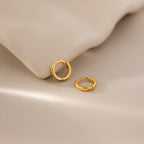 Pair of 6mm tiny classic gold huggie hoop earrings resting on a neutral surface, styled beside a smooth ceramic dish.
