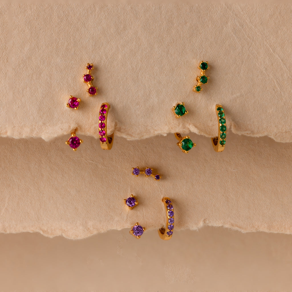 Opal Earring Trio Set—gold earrings with colorful red, green, and purple gemstones—displayed on textured beige paper. These birthstone earrings add vibrant style to any outfit.