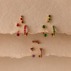 Opal Earring Trio Set—gold earrings with colorful red, green, and purple gemstones—displayed on textured beige paper. These birthstone earrings add vibrant style to any outfit.