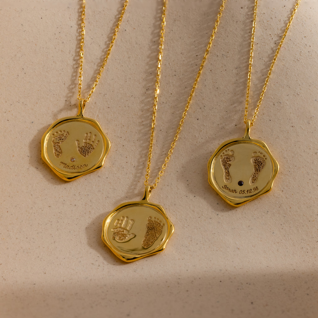 The Baby Hand & Footprint Necklace in 18K Gold features three round pendants engraved with baby handprints, footprints, and custom text—an ideal keepsake or personalized gift for new parents.