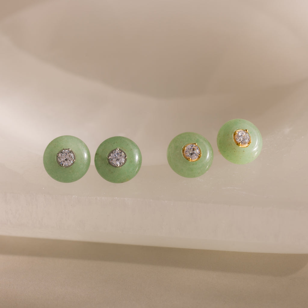 Close-up of two pairs of round green jade stud earrings in gold and silver, each featuring a sparkling CZ diamond center, displayed on a neutral background.