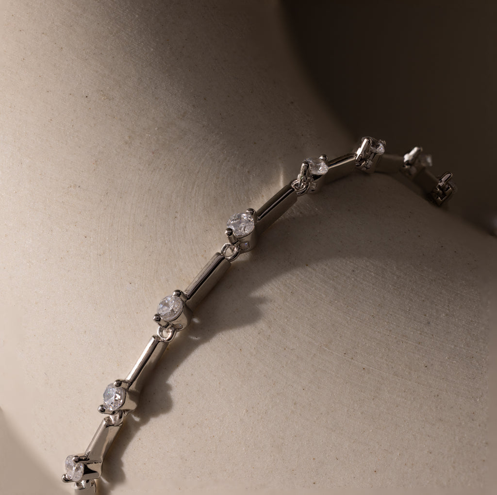 Sprinkle Diamond Tennis Bracelet in Silver displayed on a smooth, light beige surface in soft lighting.