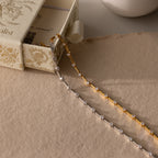 Two delicate chain necklaces—one gold, one silver—shown beside an ornate cream box, pair perfectly with the Sprinkle Diamond Tennis Bracelet in 18K Gold.