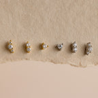 Six pairs from the Tiny Diamond Flatback Studs Set, in gold and silver, are arranged on a textured beige background, highlighting these elegant studs as the perfect accessory for any occasion.