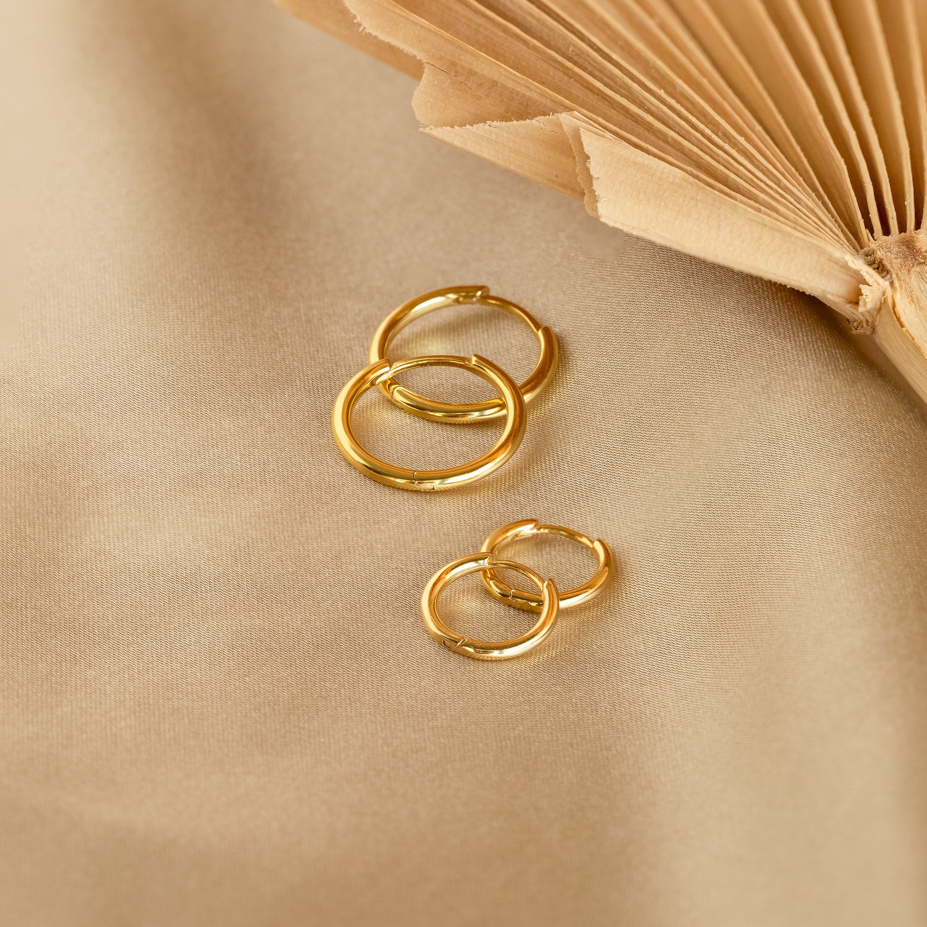 Four Medium Bold Hoops rest on beige fabric beside an open book—stylish, lightweight earrings perfect for your everyday jewelry collection.