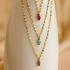 Three gold chain Custom Marquise Birthstone Necklaces with marquise-cut red, blue, and purple gemstones are displayed on a white stand—an eye-catching gift or personalized birthstone necklace.