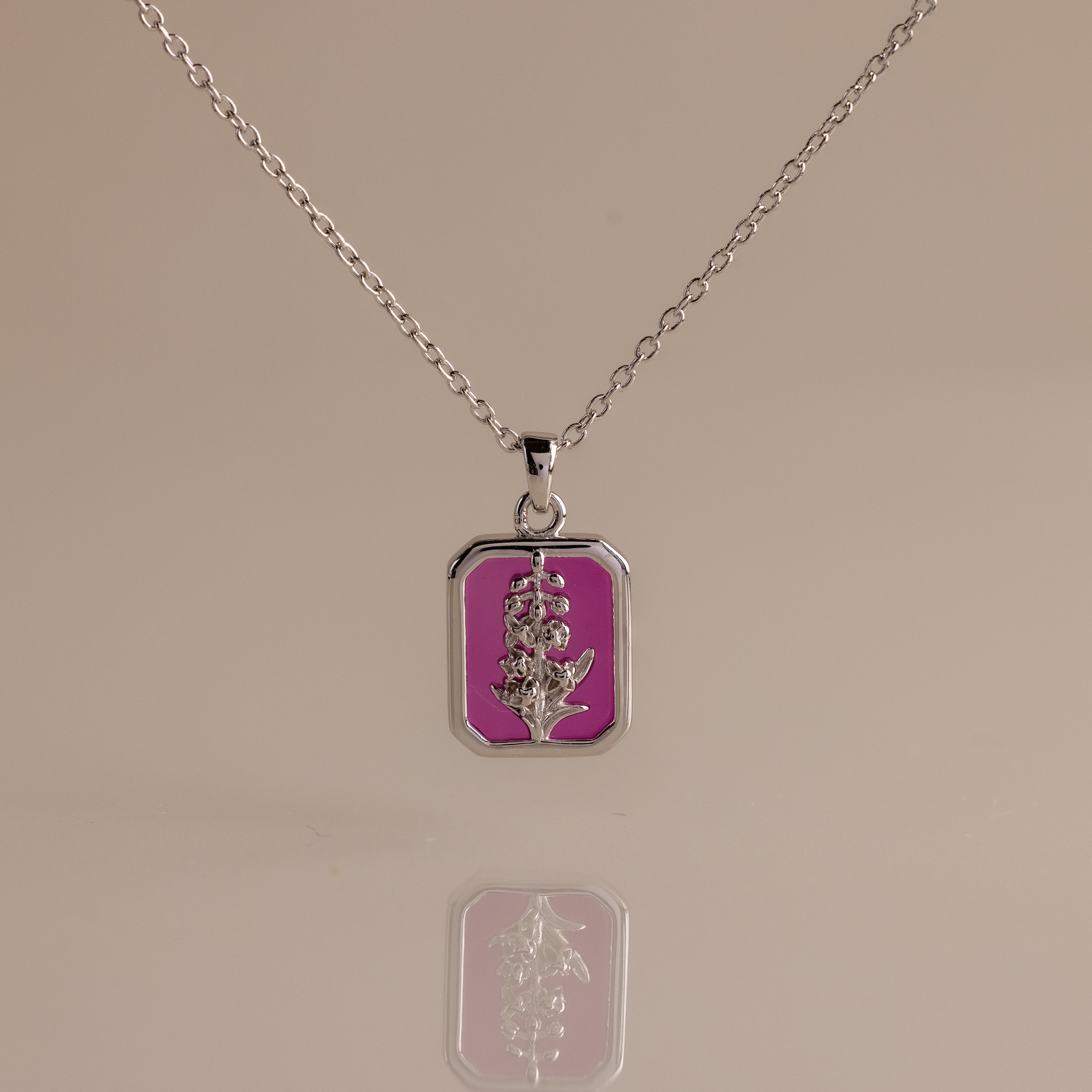 Ruby Birth Flower Charm Necklace with a rectangular pendant showcases a flower design on a pink background, mirrored below.
