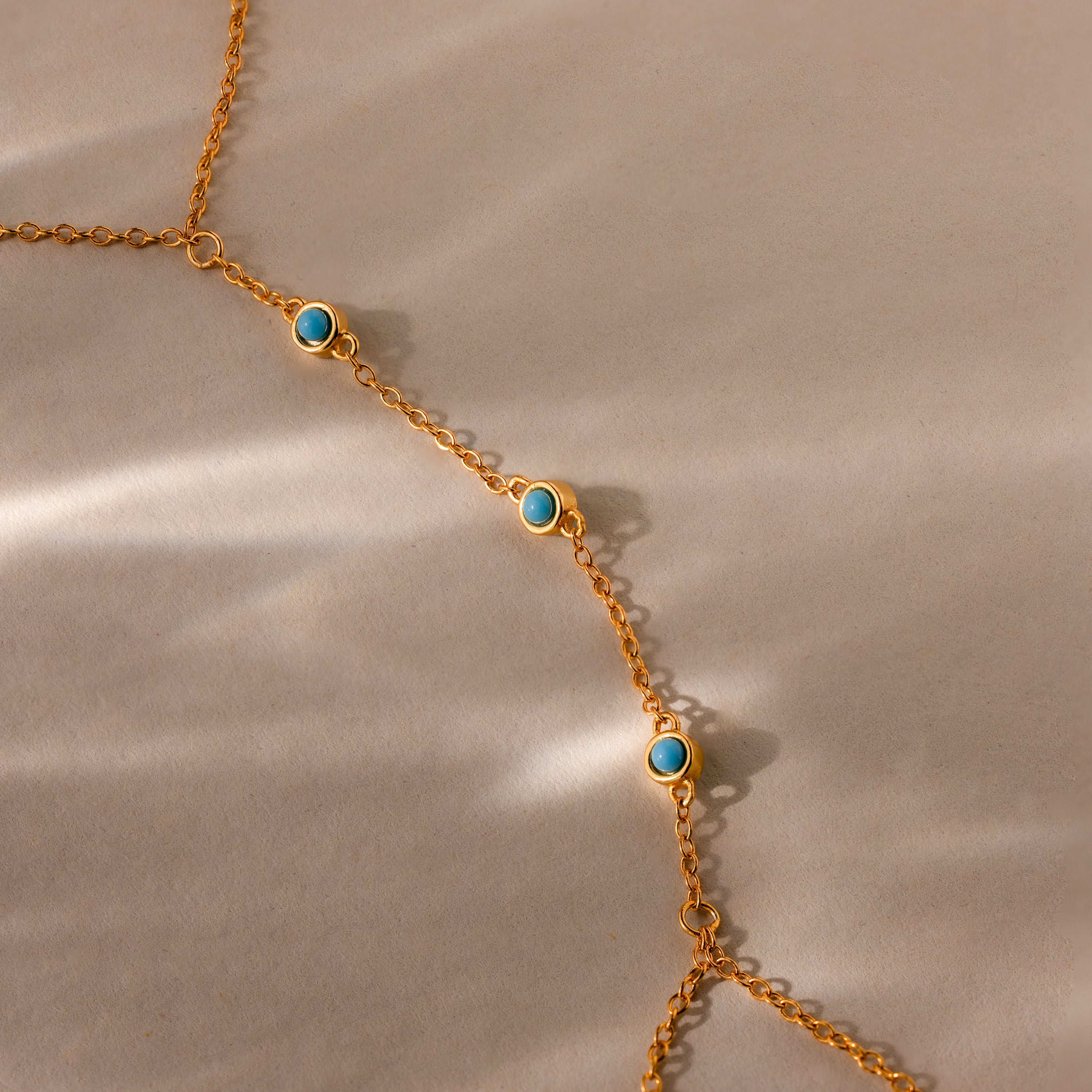 Turquoise Hand Chain Bracelet featuring a gold delicate chain with small turquoise stones, displayed diagonally on a beige background with soft shadows.