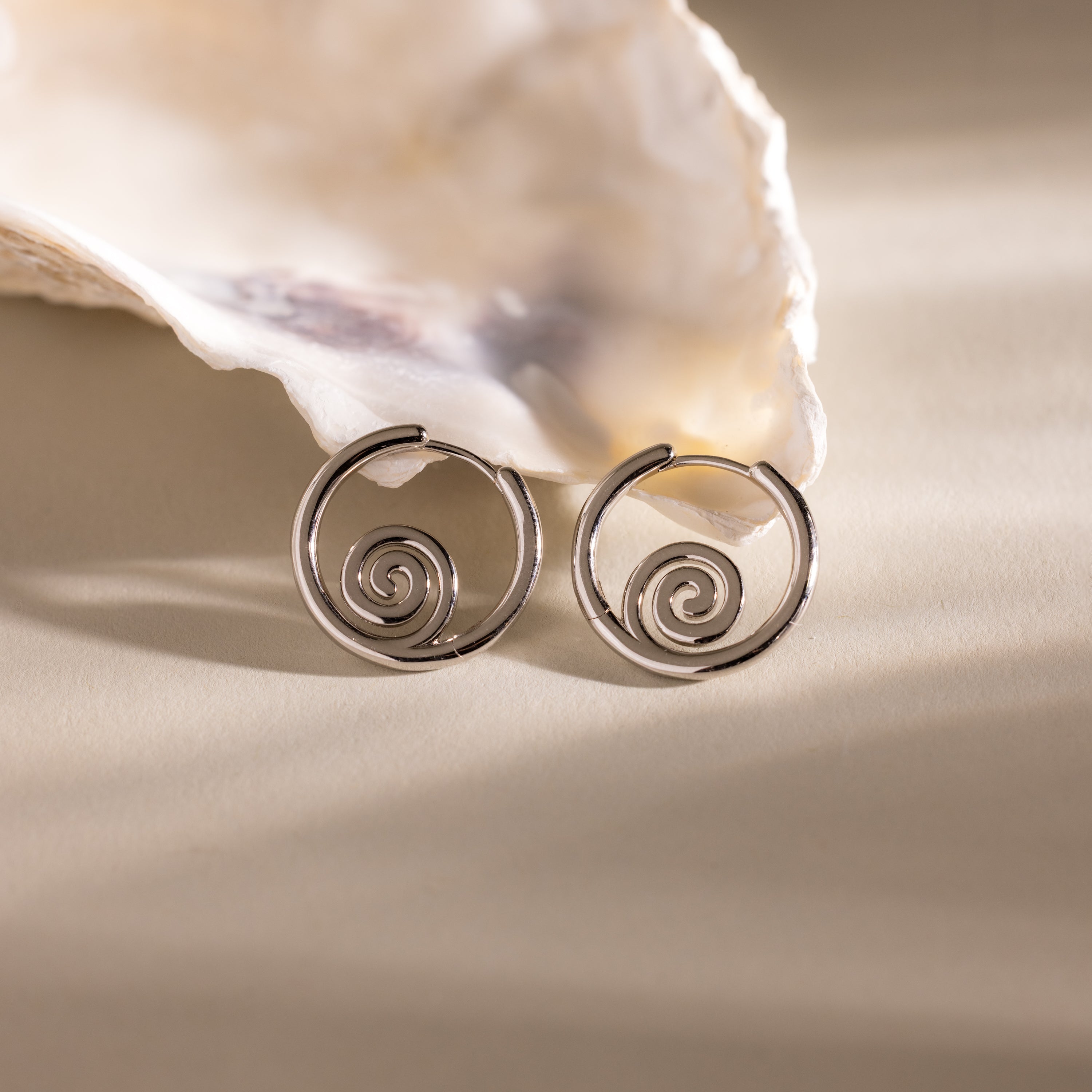 Spiral Swirl Hoops shown in front of a seashell on a beige surface with soft lighting—stylish earrings to enhance your boho vacation outfits.