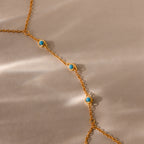 The Turquoise Hand Chain Bracelet in 18K Gold features delicate turquoise stones and is displayed against a neutral beige background with gentle light reflections.
