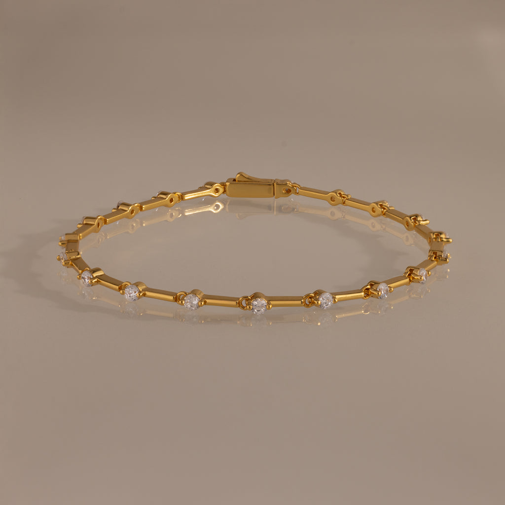The Sprinkle Diamond Tennis Bracelet in 18K Gold features evenly spaced round diamonds, elegantly displayed on a neutral reflective surface.