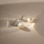 The Diamond Pearl Droplet Earrings rest on a beige surface, illuminated by soft sunlight and gentle shadows.
