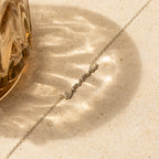 Dainty Bubble Name Necklace displayed on a beige stone surface with sunlight reflections, beside a glass object—perfect personalized nameplate for your custom jewelry collection.