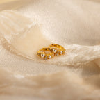 The Pearl Diamond Cluster Huggies in 18K Gold, featuring pearls and diamond accents, are displayed on soft, cream-colored fabric.