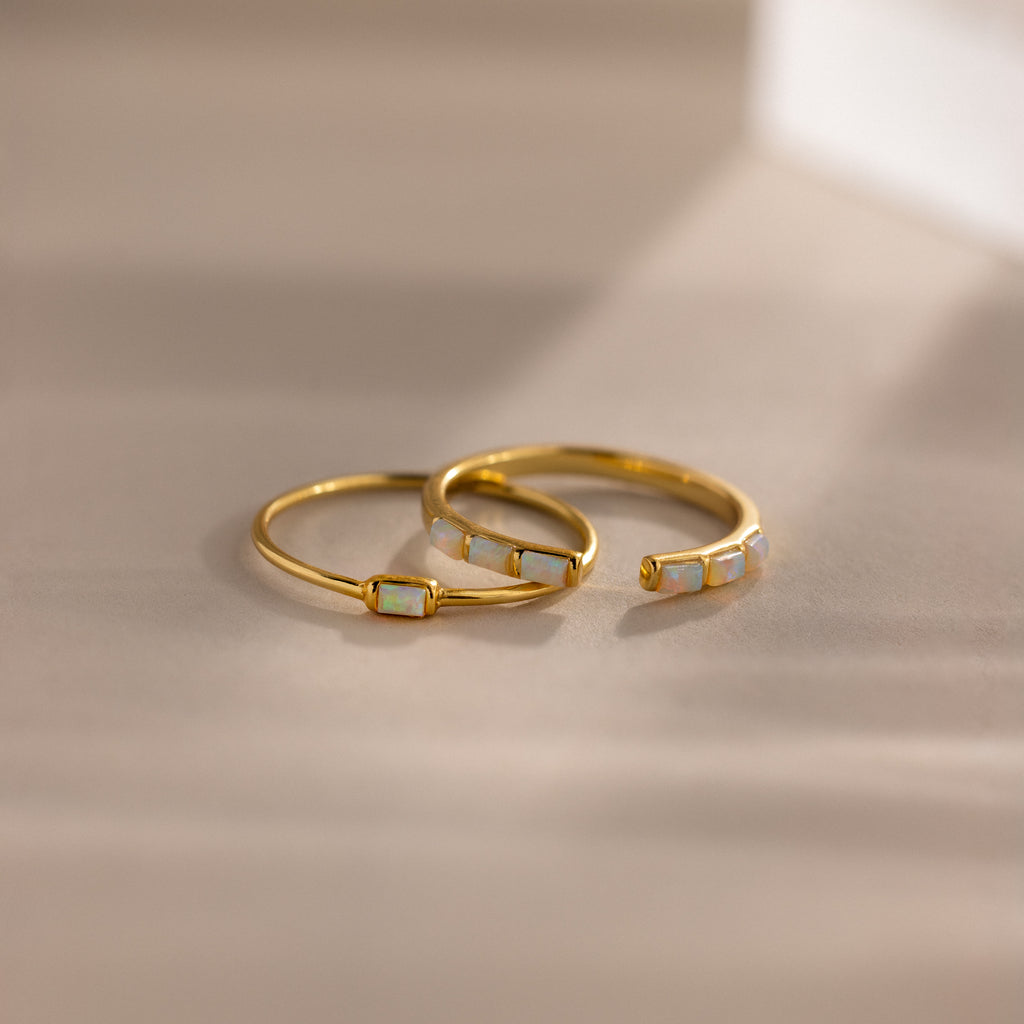 Minimalist gold ring set with baguette-cut opals — one with a single opal and the other with five opals in a row, shown in soft natural light.