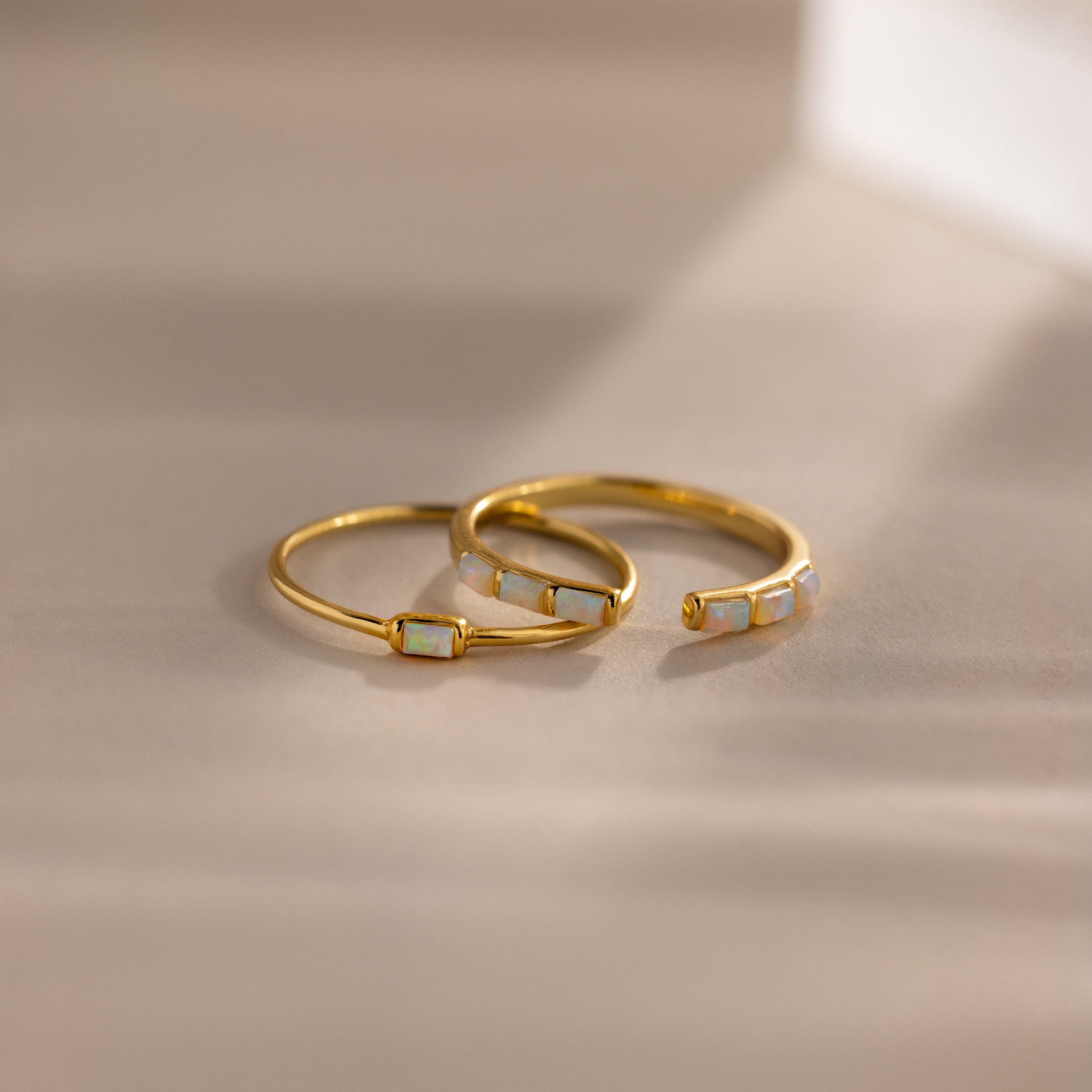 Minimalist gold ring set with baguette-cut opals — one with a single opal and the other with five opals in a row, shown in soft natural light.