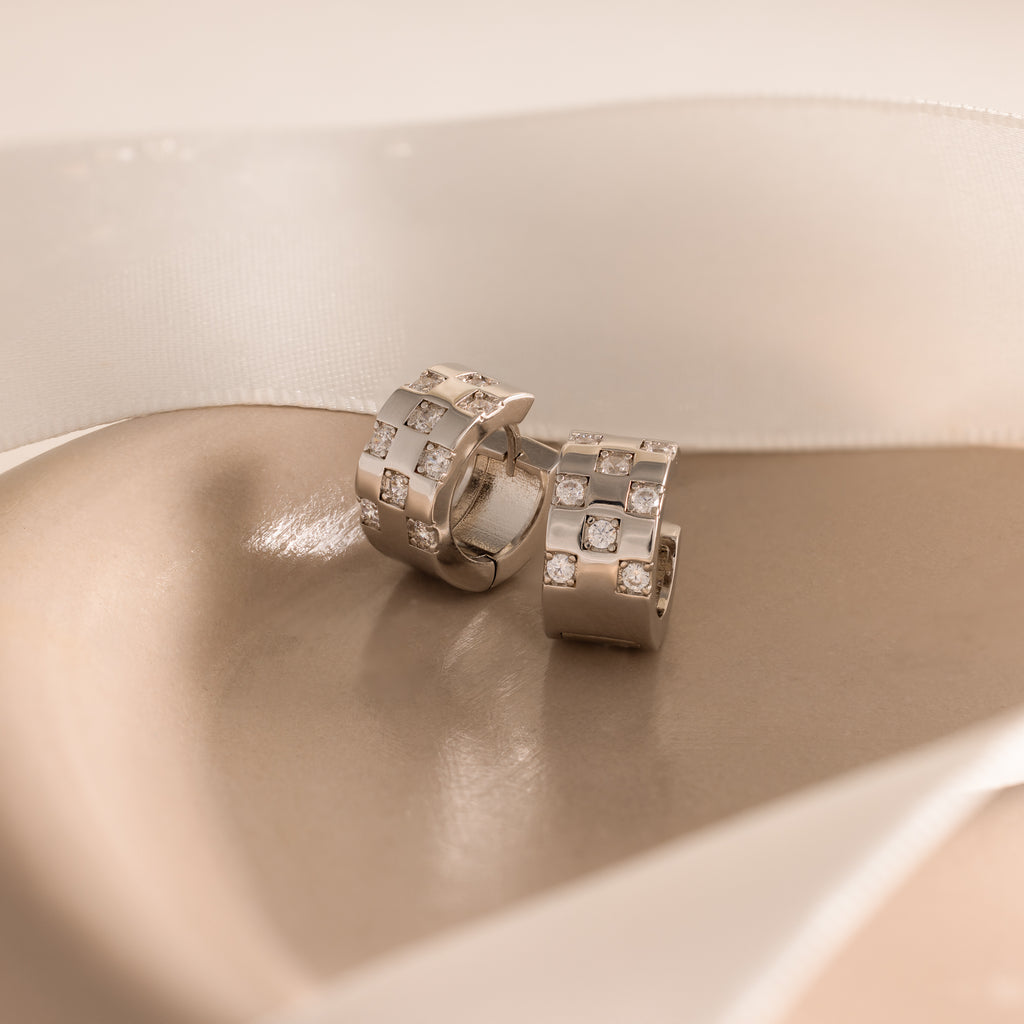 Pave Checkered Huggies, featuring a small diamond checkered pattern, displayed on a soft beige background with ribbon.