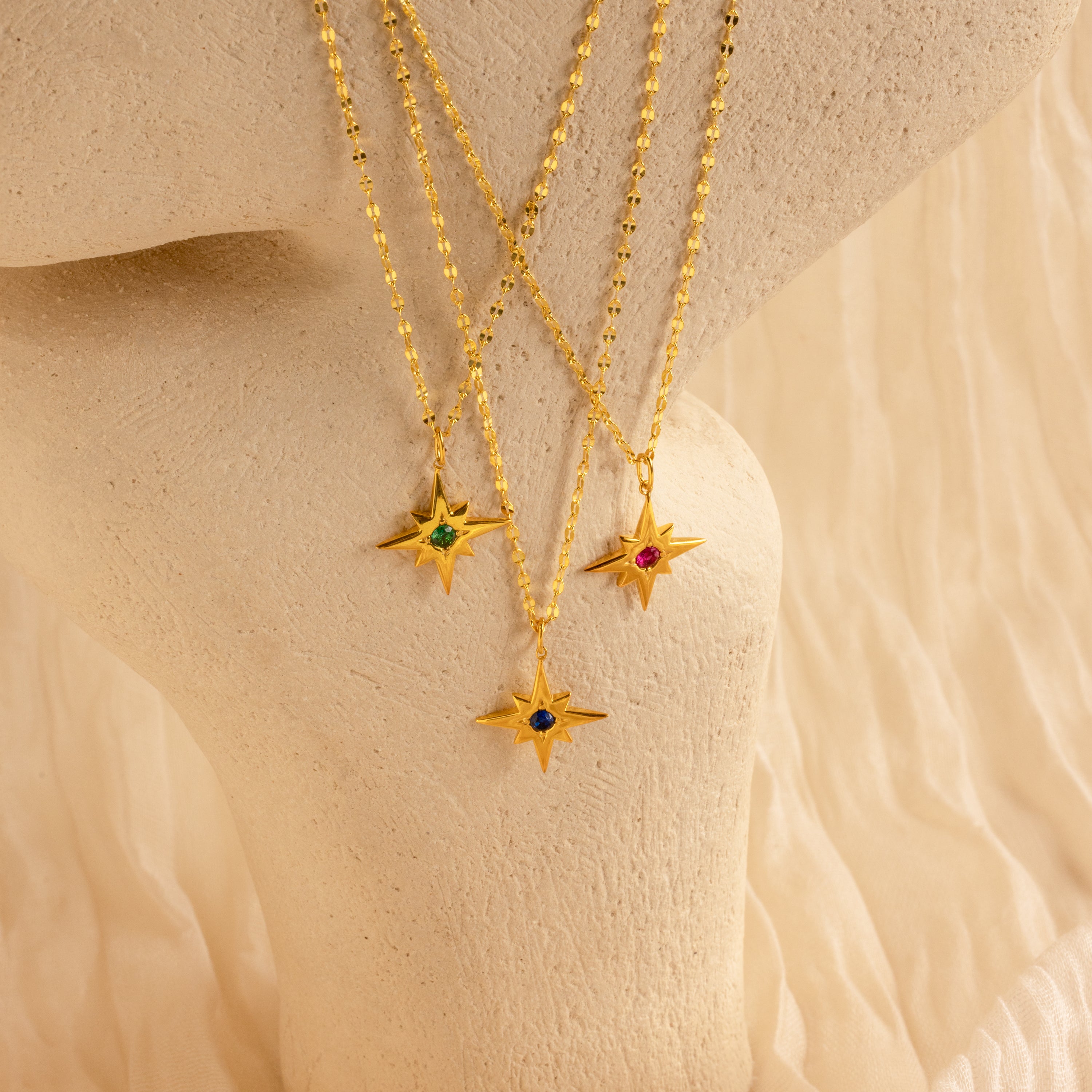 Three Star Birthstone Necklaces featuring colored gemstones are displayed on a textured cream surface—an ideal piece of celestial jewelry and a perfect personalized gift.