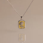 The Topaz Birth Flower Charm Necklace features a rectangular sunflower pendant, beautifully displayed on a beige background with an elegant reflection—ideal for those seeking a unique and delicate jewelry statement.