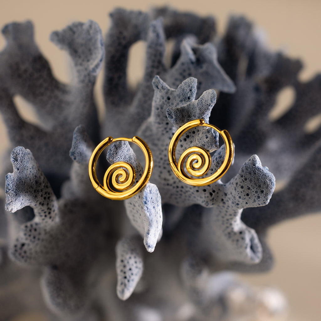 Spiral Swirl Hoops in 18K Gold shown on textured gray coral—stylish boho vacation jewelry for anyone looking for unique, beachy earrings.