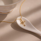 A Vintage Diamond Cross Necklace in 18K Gold rests on a white ceramic spoon beside a teacup.