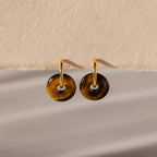 Tiger's Eye Duo Hoops: gold hoop earrings with round Tiger's Eye stone pendants, elegantly displayed on a textured beige background.