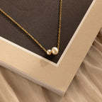 The Dainty Duo Pearl Necklace in 18K Gold, featuring two pearls on a textured beige and brown background, is perfect as wedding jewelry or a thoughtful gift for someone special.