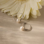 Round Pearl Hoops in Sterling Silver, featuring luminous pearls on polished silver hoops, are displayed on a light surface next to a large cream flower.