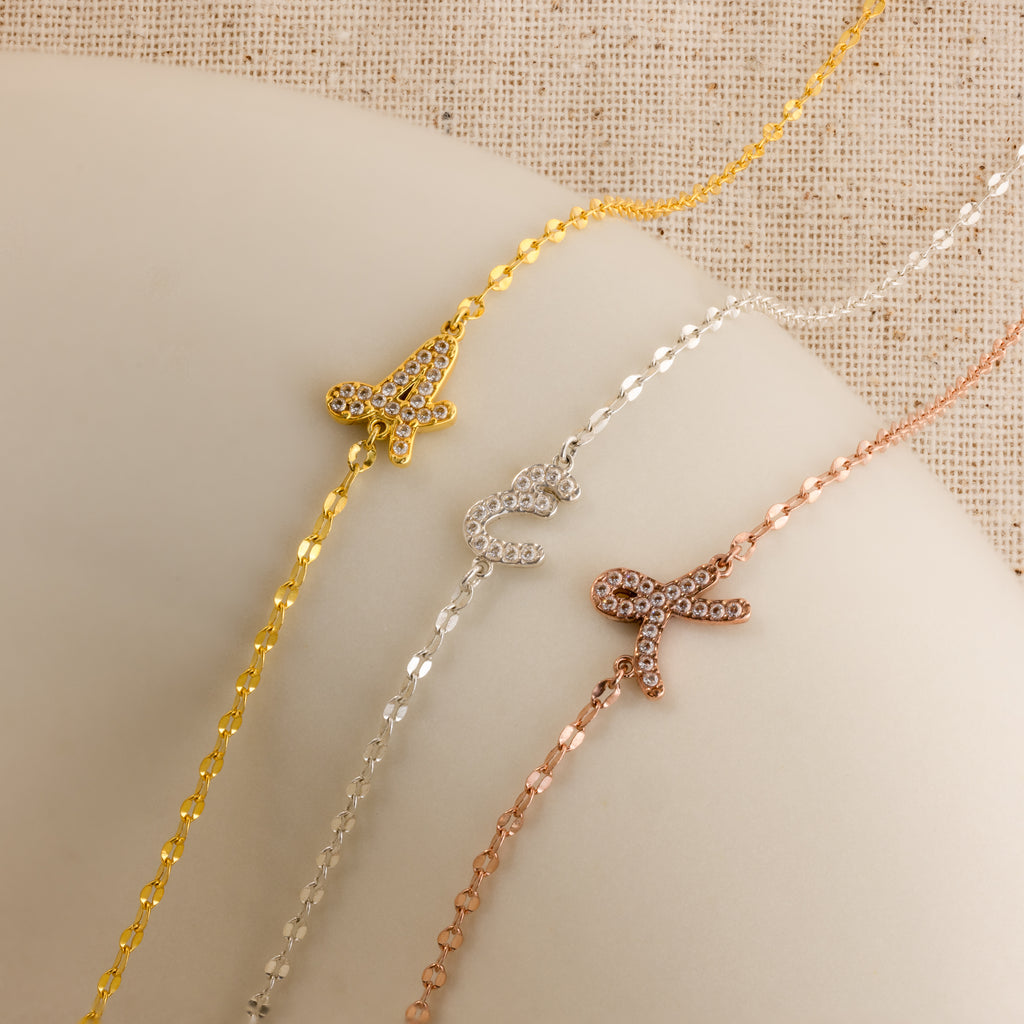 The Nella Pave Off-Center Initial Necklace features a jeweled letter charm on a delicate chain in gold, silver, or rose gold—perfect for fans of the initial necklace trend.