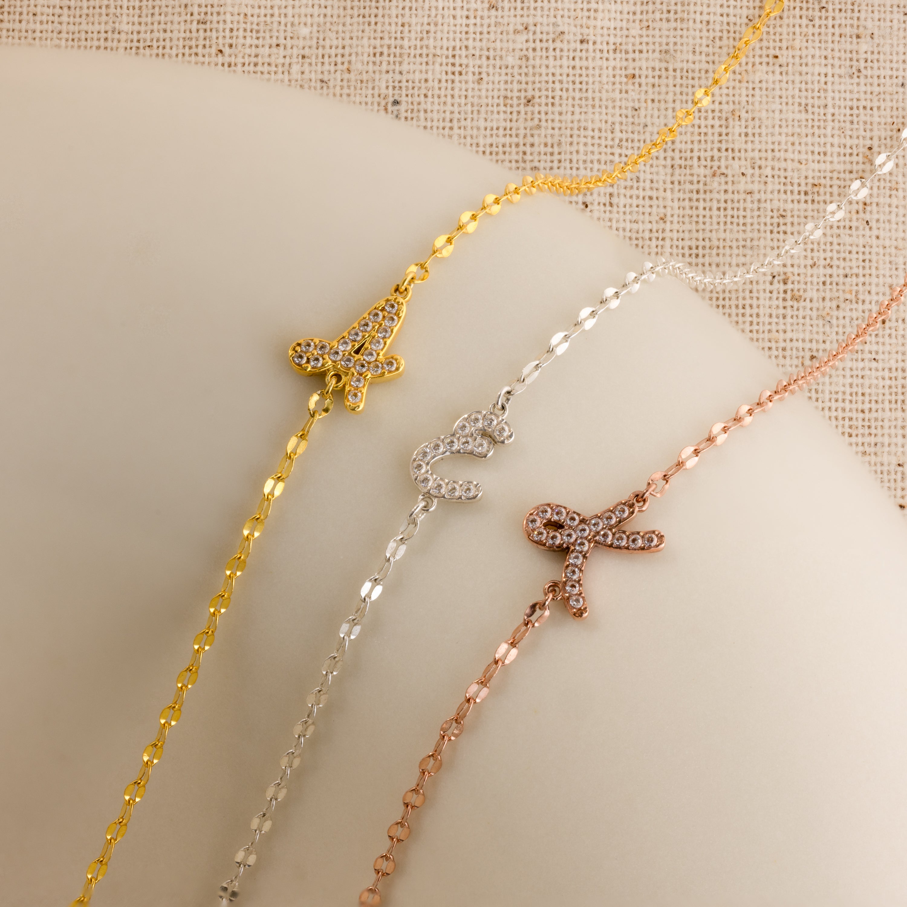 The Nella Pave Off-Center Initial Necklace features a jeweled letter charm on a delicate chain in gold, silver, or rose gold—perfect for fans of the initial necklace trend.