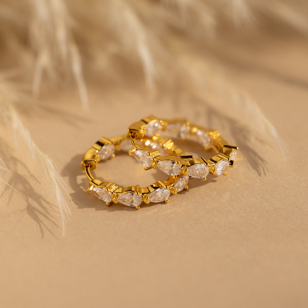 Inside Out Pear Diamond Hoops featuring marquise-cut CZ stones, shown on a beige surface with a softly blurred background.