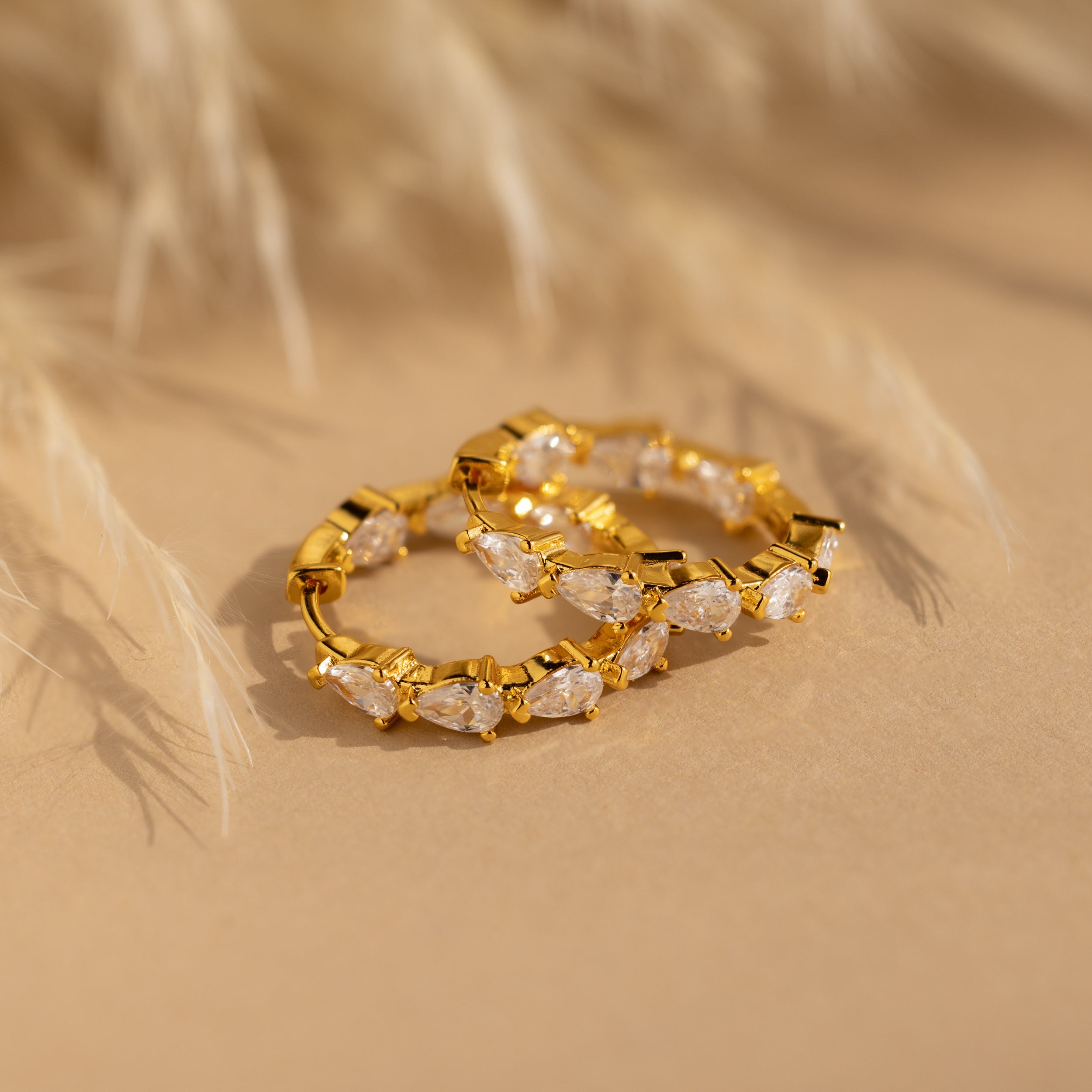 Inside Out Pear Diamond Hoops featuring marquise-cut CZ stones, shown on a beige surface with a softly blurred background.