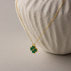 18K gold necklace with a green malachite gemstone clover pendant on a delicate chain against a neutral background.
