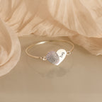 The Fingerprint Heart Bangle is a silver bracelet with a heart charm engraved with a fingerprint and "Dad," making it a unique personalized gift.