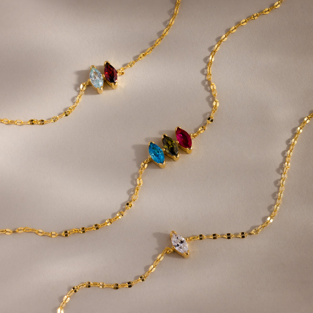 The Multiple Marquise Birthstone Bracelet features marquise-cut gemstones in blue, green, red, and clear, evoking birthstone elegance and beautifully displayed on a beige background.