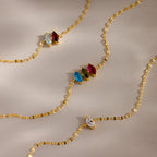 The Multiple Marquise Birthstone Bracelet features marquise-cut gemstones in blue, green, red, and clear, evoking birthstone elegance and beautifully displayed on a beige background.