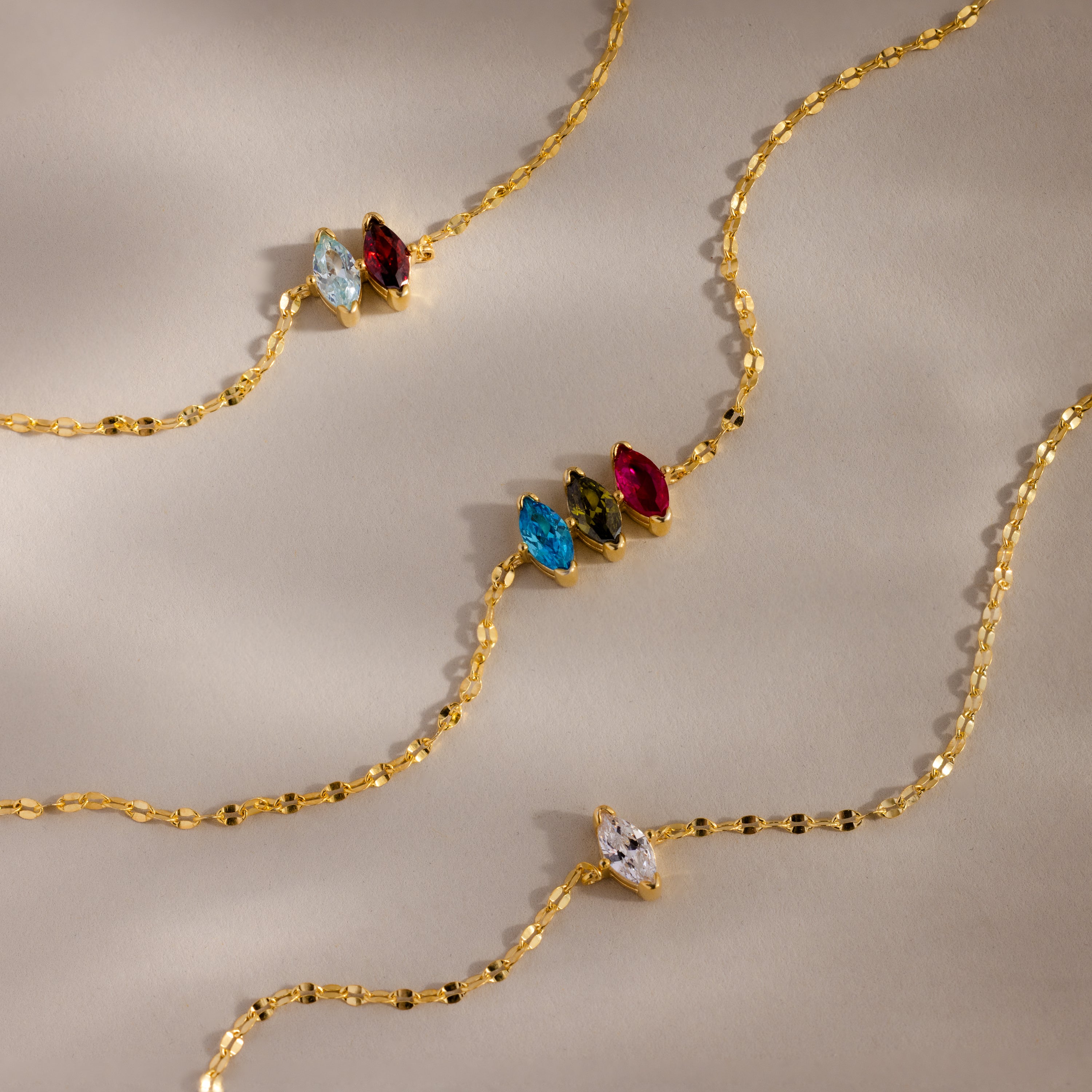 The Multiple Marquise Birthstone Bracelet features marquise-cut gemstones in blue, green, red, and clear, evoking birthstone elegance and beautifully displayed on a beige background.