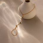 The Turquoise Hand Chain Bracelet in 18K Gold is elegantly draped over a white vase, illuminated by sunlight.