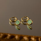 Jade Drop Hoops in 18K Gold, featuring round jade gemstones, displayed on a reflective brown surface.