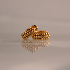 The Beaded Chunky Hoops in 18K Gold, featuring beaded detailing, are displayed on a reflective surface against a soft, neutral background.