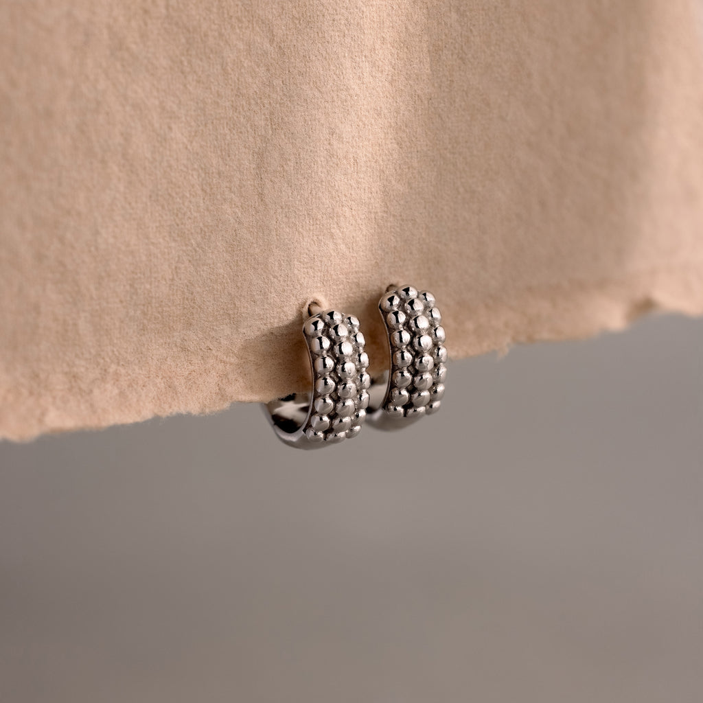 Beaded Chunky Hoops in Sterling Silver rest on a beige paper edge, showcasing a modern, textured design ideal for elevating any contemporary style.