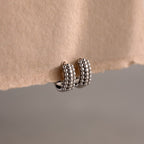 Beaded Chunky Hoops in Sterling Silver rest on a beige paper edge, showcasing a modern, textured design ideal for elevating any contemporary style.