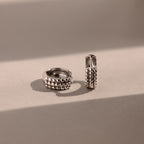 The Beaded Chunky Hoops in Sterling Silver, featuring a textured and beaded design, are displayed on a neutral surface, blending modern style with classic elegance.