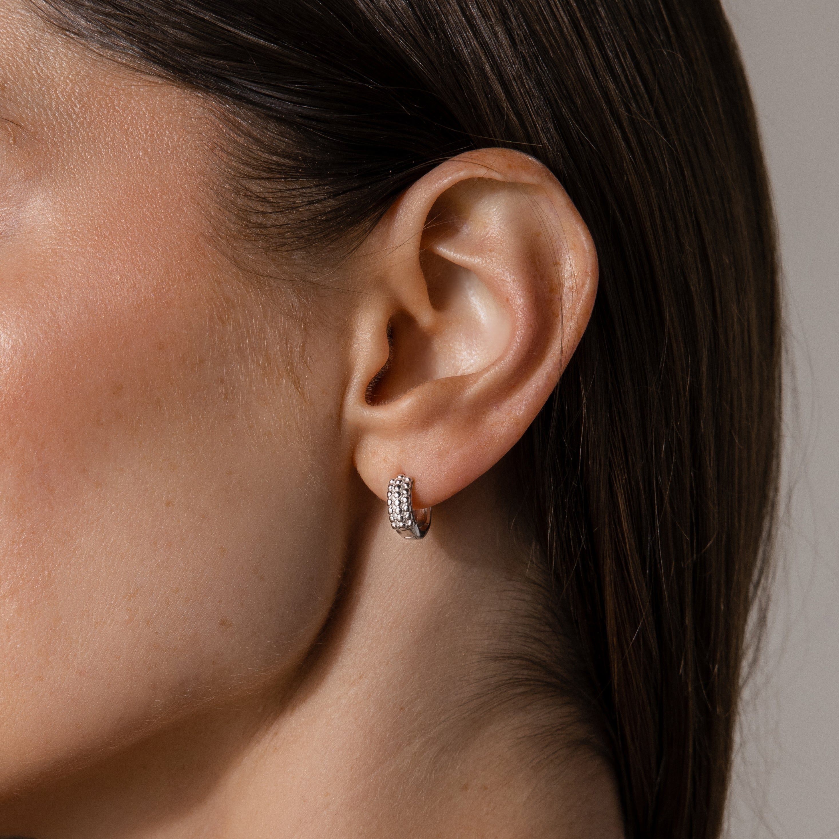 Close-up of a woman's ear wearing Beaded Chunky Hoops in Sterling Silver—modern, small silver hoops with embedded sparkling stones.