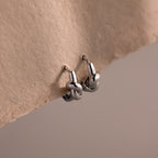 Love Knot Huggies in Sterling Silver are shown on textured beige paper against a soft, neutral background—an ideal, meaningful gift to celebrate lasting bonds.