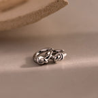 A pair of Love Knot Huggies in Sterling Silver rests on a smooth, neutral surface—an ideal, meaningful gift symbolizing lasting bonds.