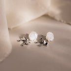 White rose and silver bow earrings displayed on a neutral surface.